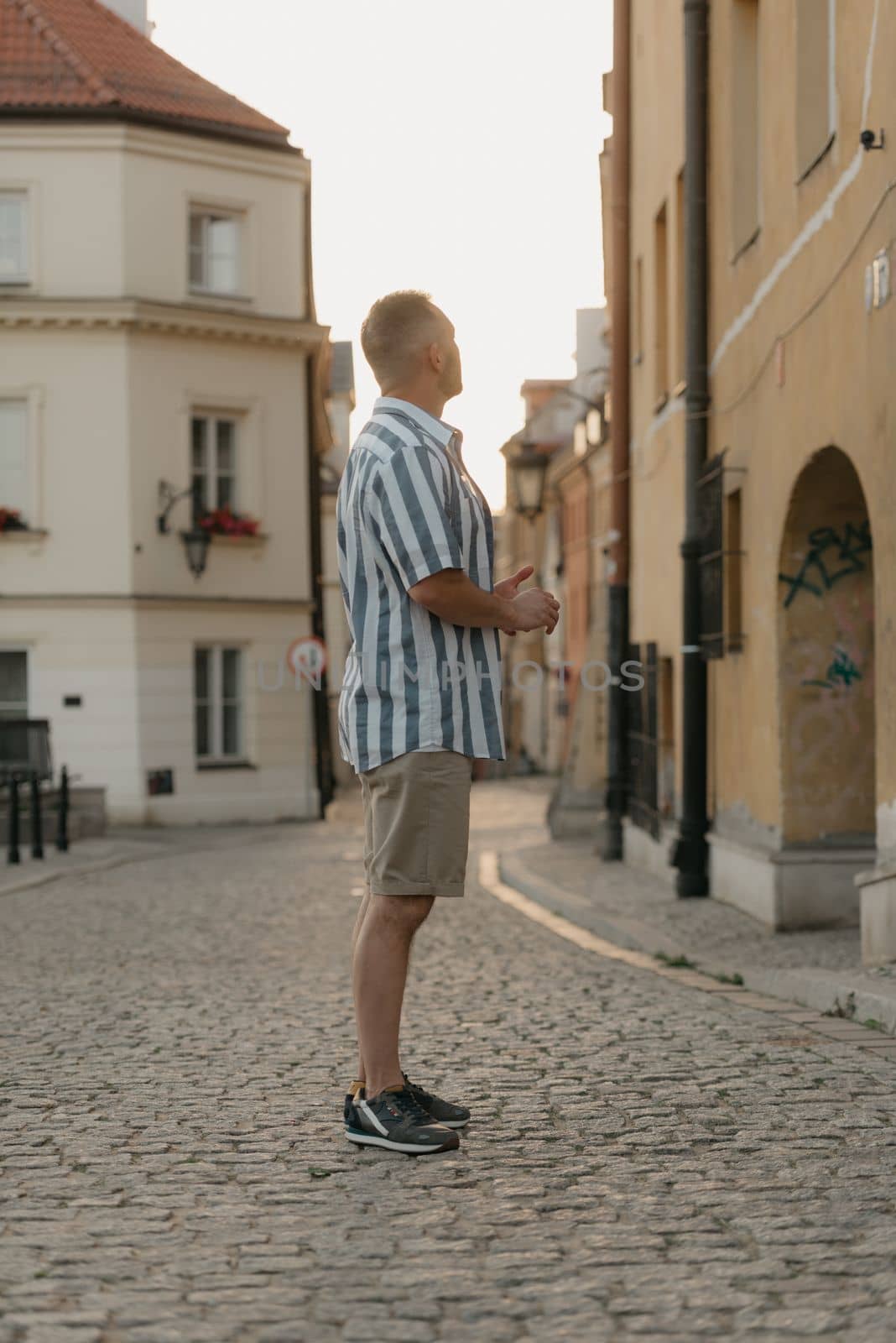 A middle-aged male tourist is looking at the sights in an old European town. A man in a shirt and shorts in Warsaw in the evening.