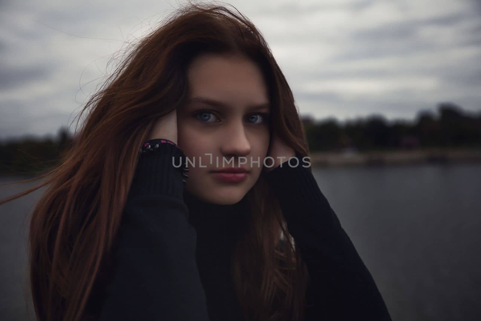 cute teenager girl straightens her facial hair near the water in the evening outdoors. High quality photo