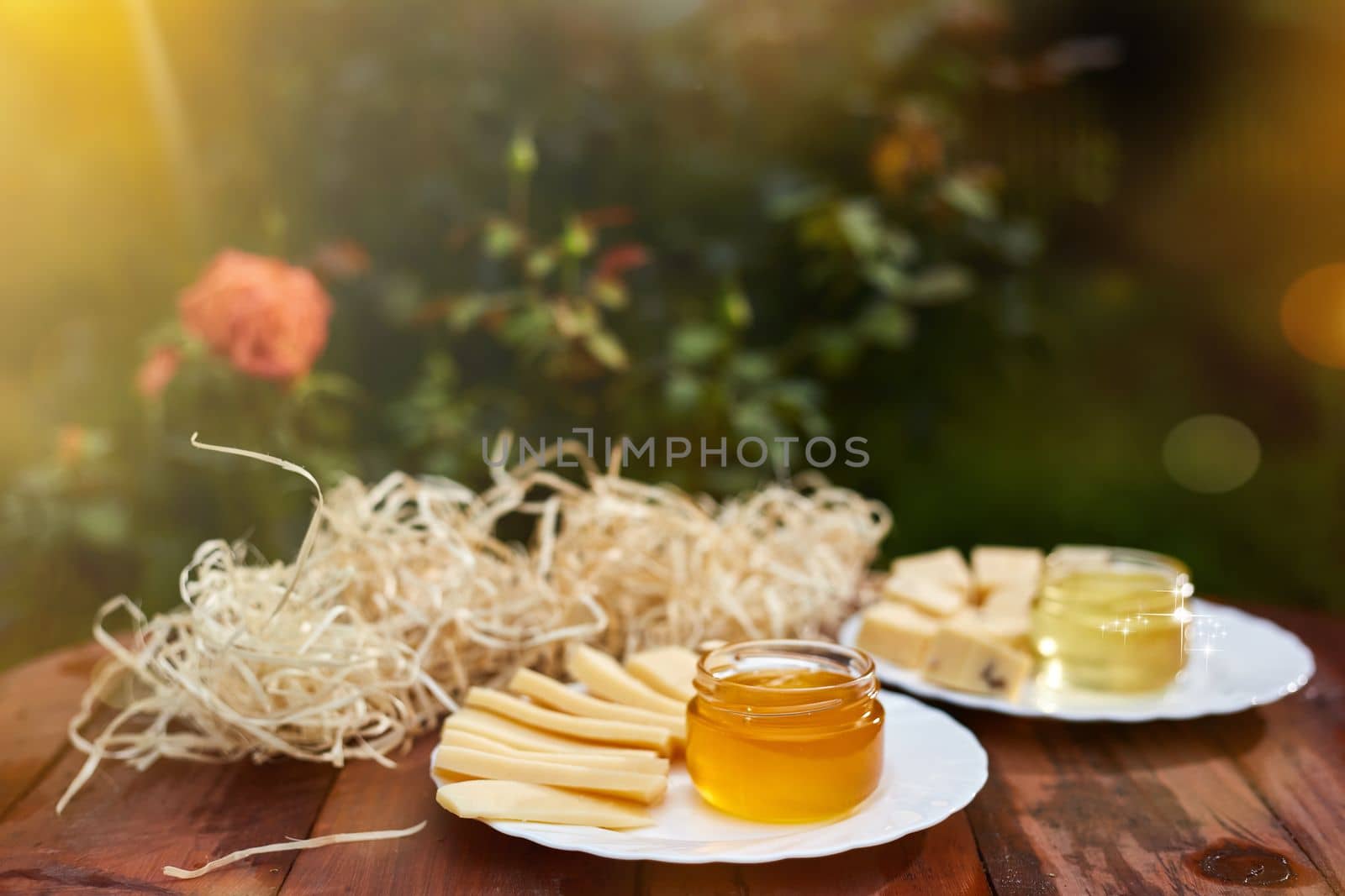 a jar of sweet honey with cheese and roses and fresh bread with bright light beautiful decoration creative photo in a bucket on a wooden table in the garden with flowers for breakfast delicious food. High quality photo