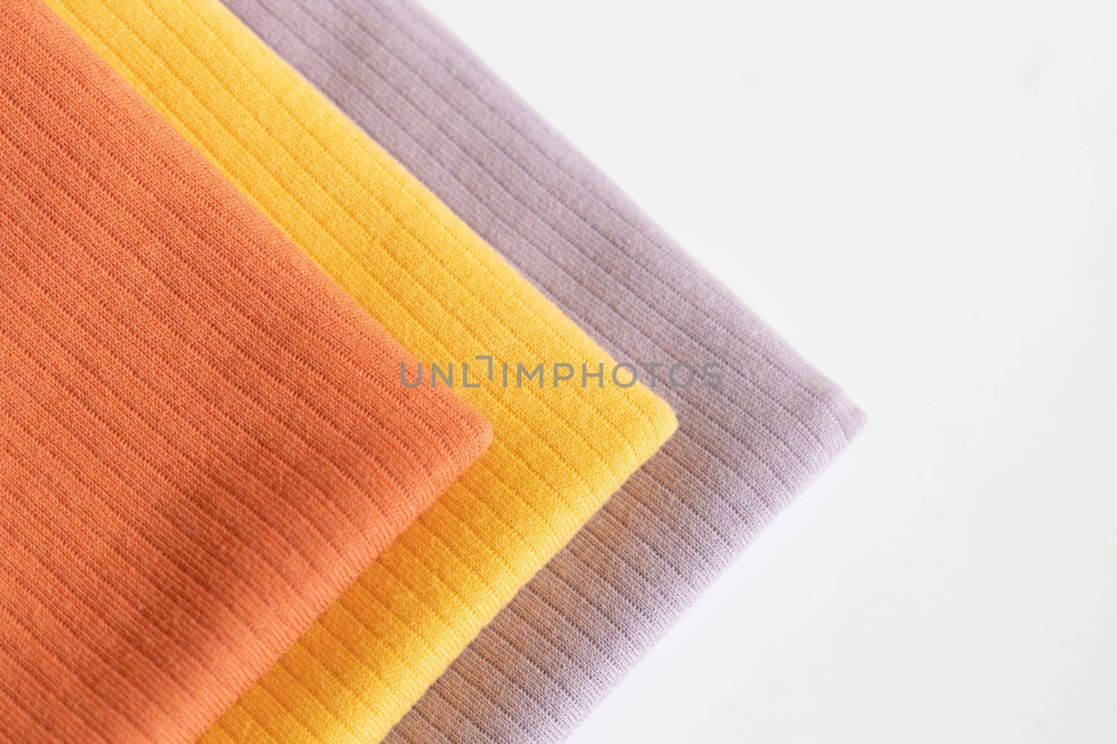 Stack folded purple, yellow baby cotton clothing on white background isolation..