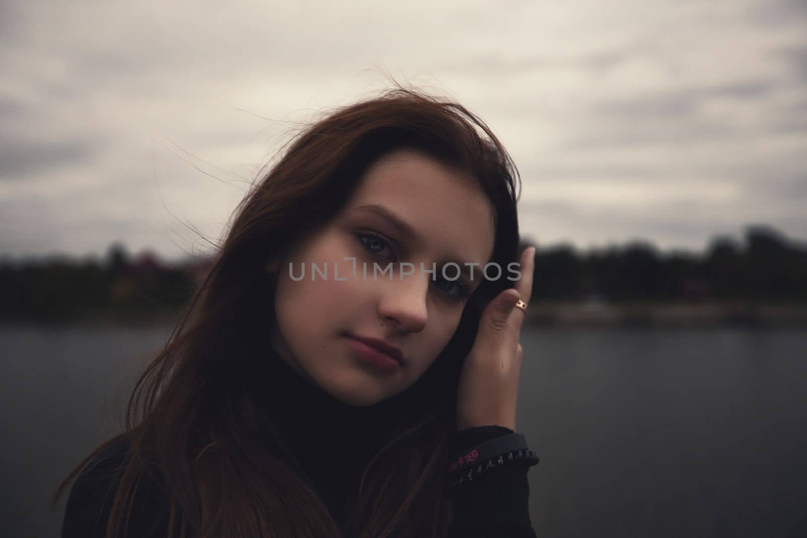 cute teenager girl straightens her facial hair near the water in the evening outdoors. High quality photo