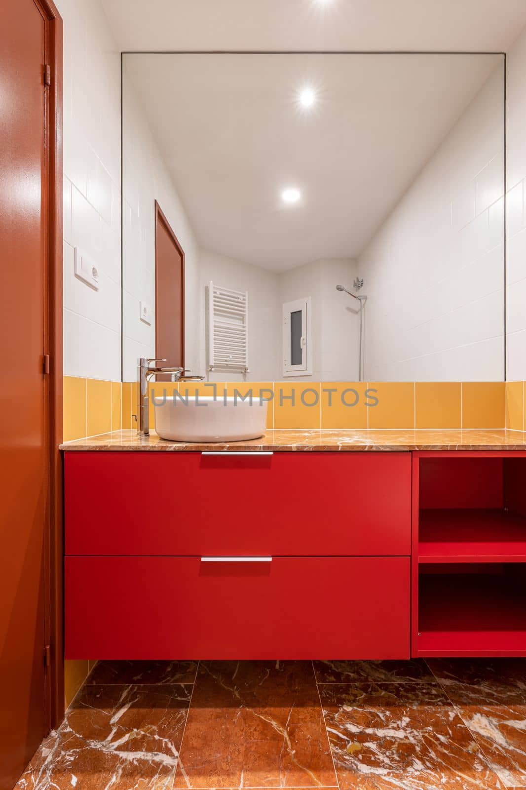 Overhead white sink on a red cabinet in a bright white and yellow bathroom White and yellow tiles on the wall and porcelain stoneware brown floor tiles. Huge bathroom wall mirror. Brown bathroom door by apavlin