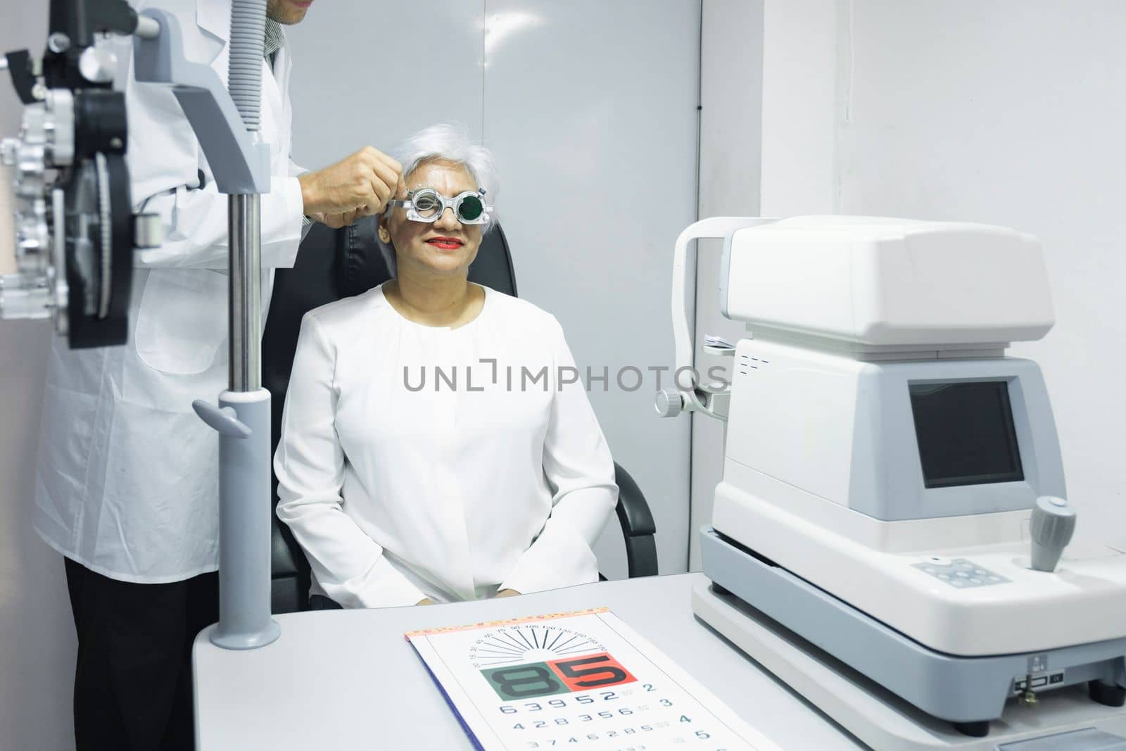 Woman sitting in optometrist cabinet having his eyesight checking, examining, testing with trial frame glasses by professional optician for new pairs of eyeglasses.