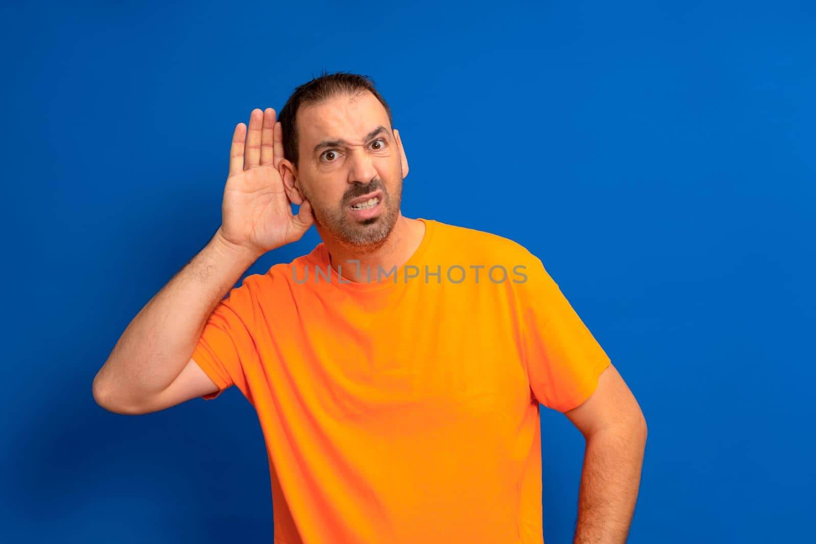 Listening man holds his hand near his ear on a blue background. Handsome man trying to listen to someone's conversation.