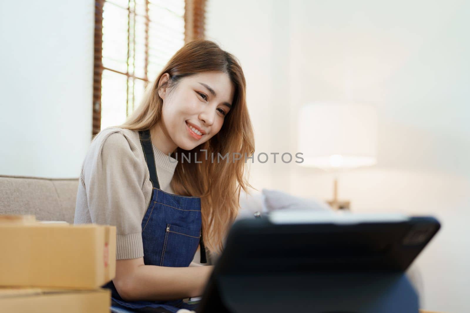 Starting small business entrepreneur of independent young Asian woman online seller is using smart phone and taking orders to pack products for delivery to customers. SME delivery concept by Manastrong