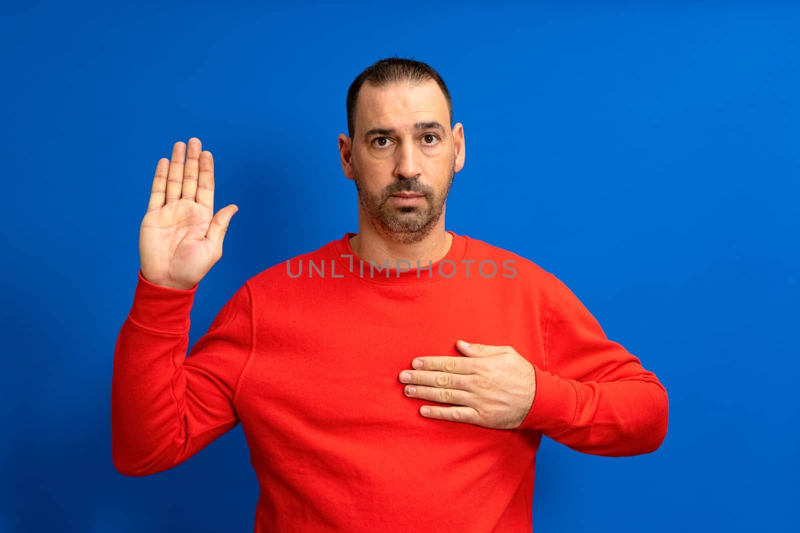 Photo of serious and confident bearded hispanic man with hand on chest promising oath isolated over blue colored background