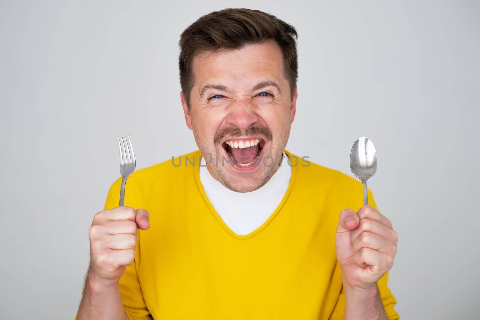 handsome hungry young man holding fork and spoon waiting for dinner. Positive facial human emotion
