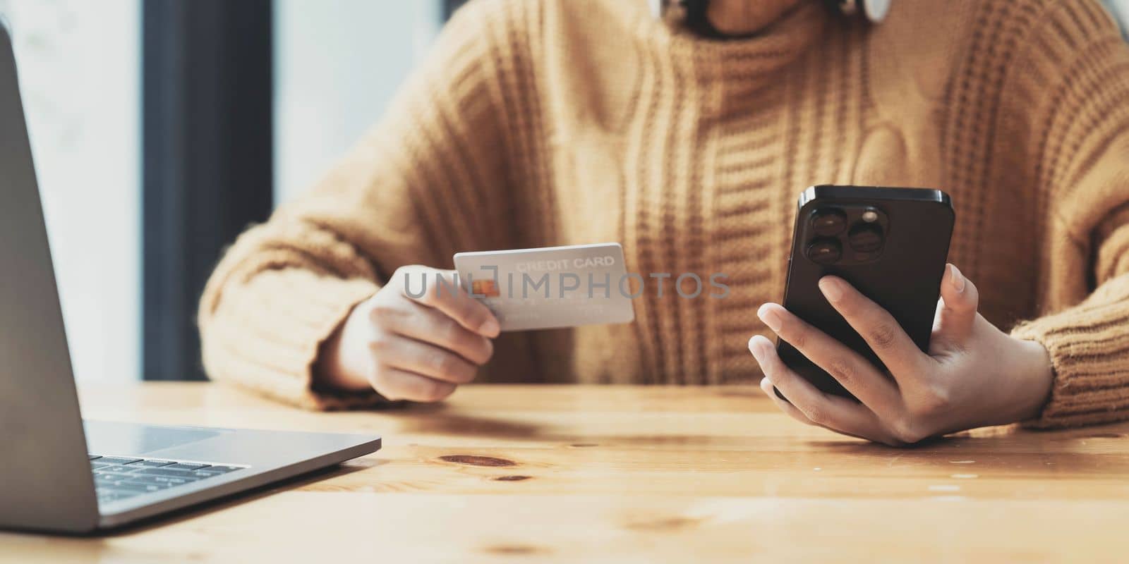 Attractive Asian female sits at her desk, holding a smartphone and a credit card. close-up image. Online payment, credit card payment, mobile banking, online shopping, cashless society...