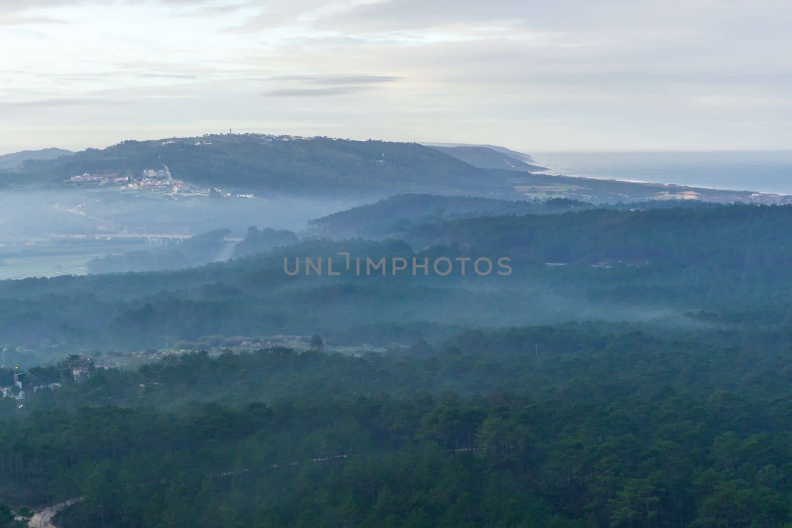 Landscape with forests in fog on the beach and village on the hill