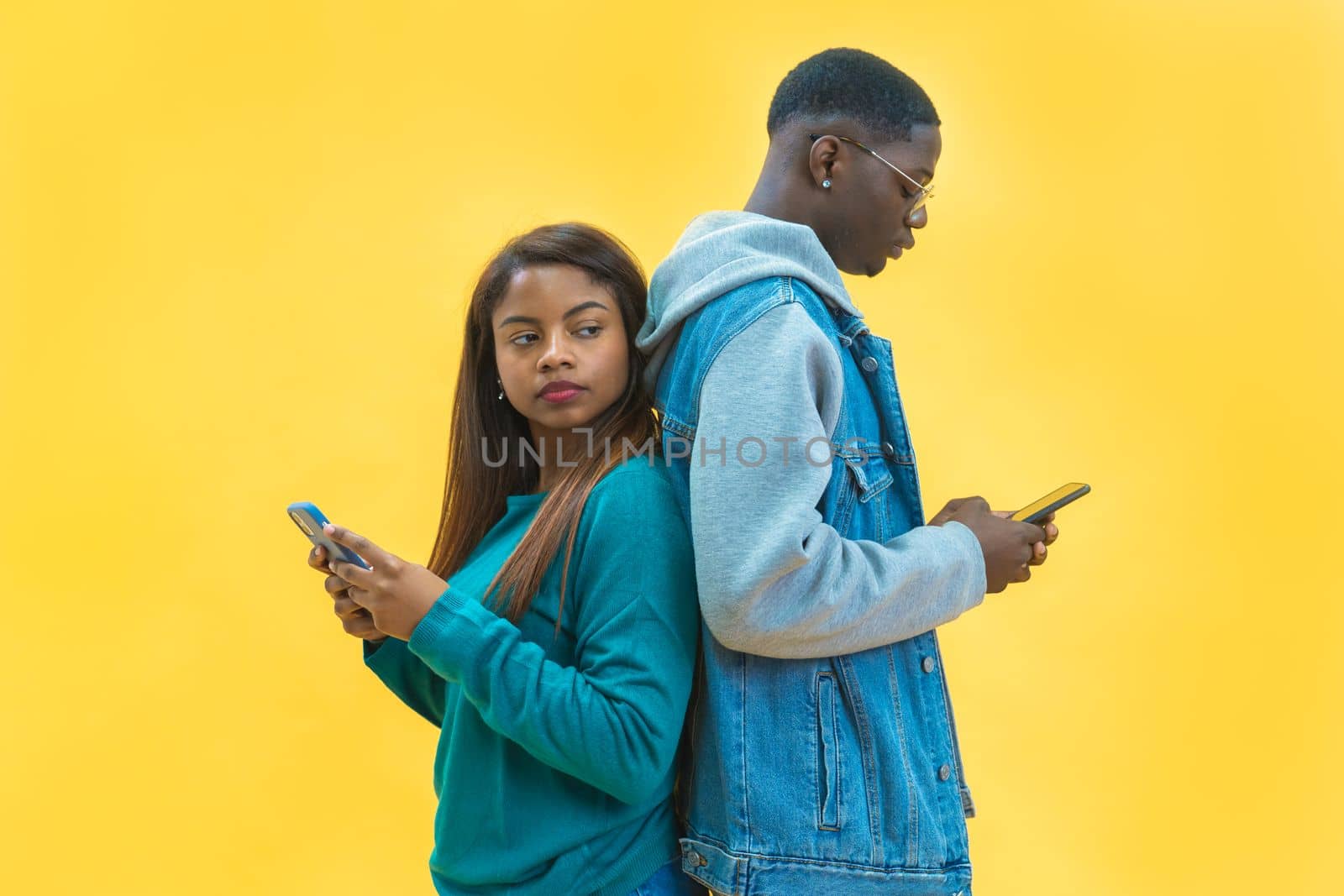 Black millennial couple using Smartphones, Standing Back To Back Yellow Background Social Network Addiction. High quality photo