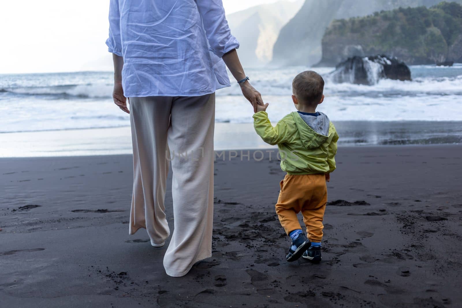 Mother and little child holding hands walking at sea side by Chechotkin