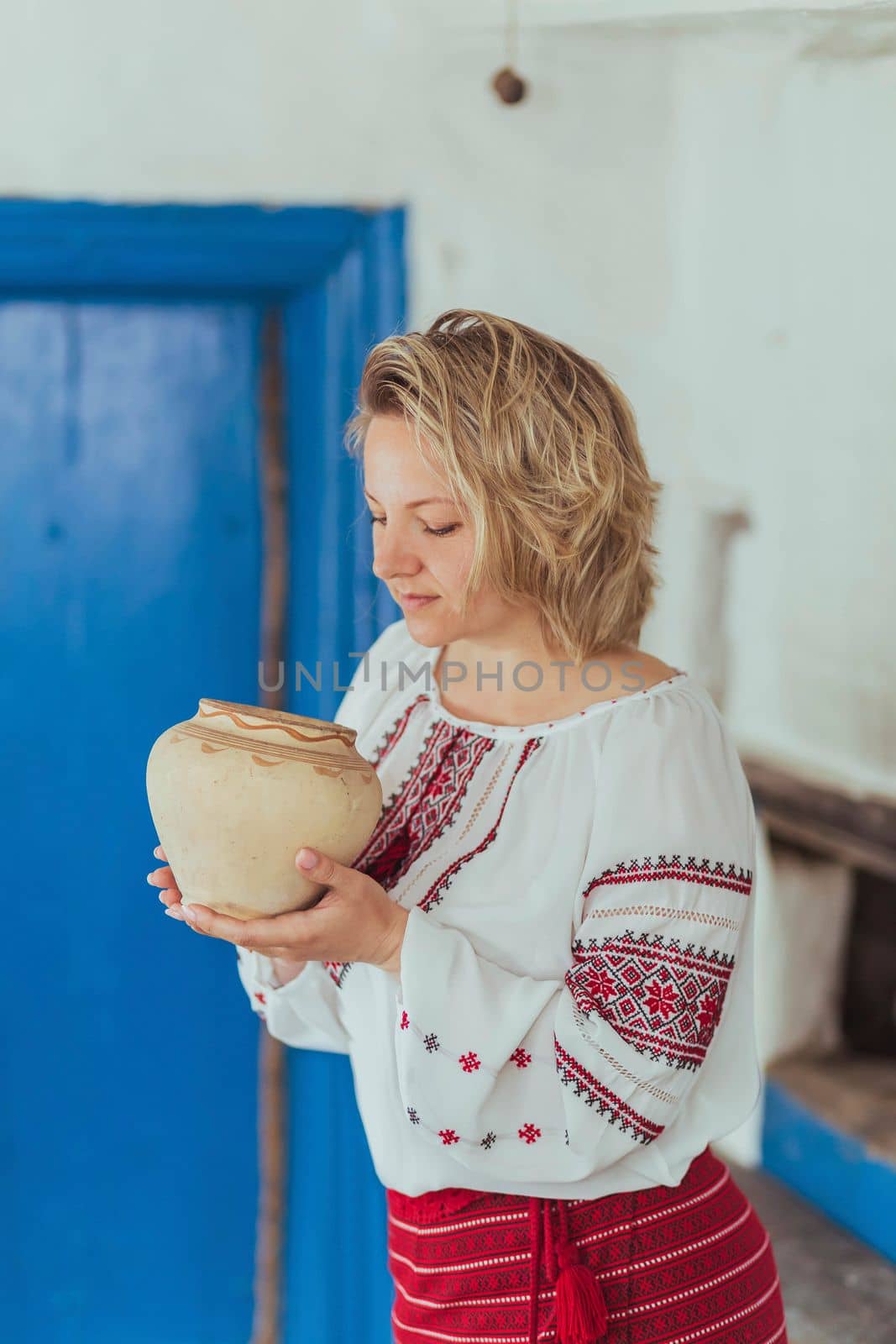 Beautiful peasant woman in embroidered clothes inhales the aroma of food in a clay pot