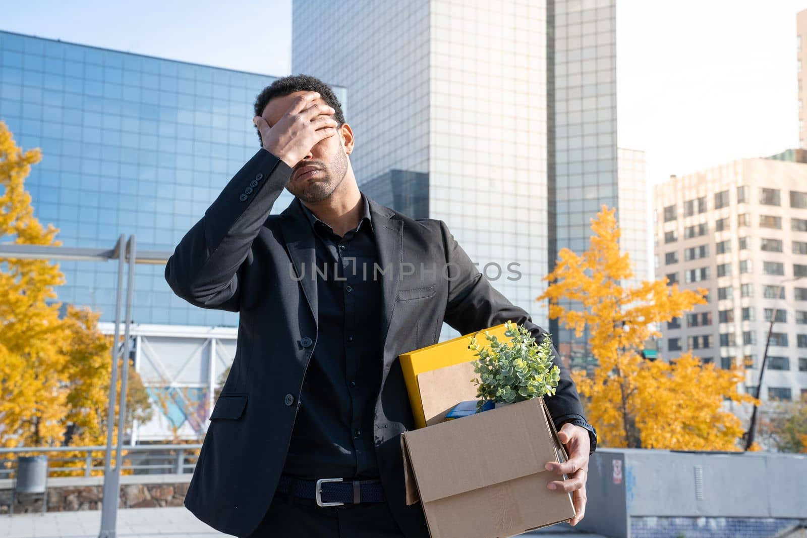 Businessman with cardboard box with office supplies standing sad outside office building. Fired concept. High quality photo