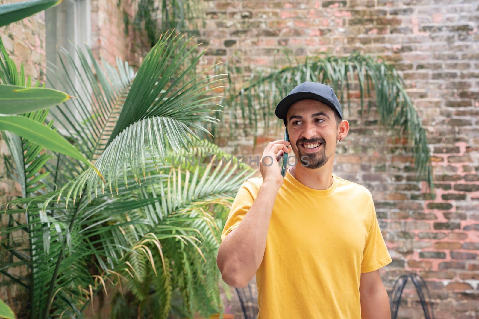 Portrait of young man talking on the phone outdoors against brick wall. Communication concept. High quality photo