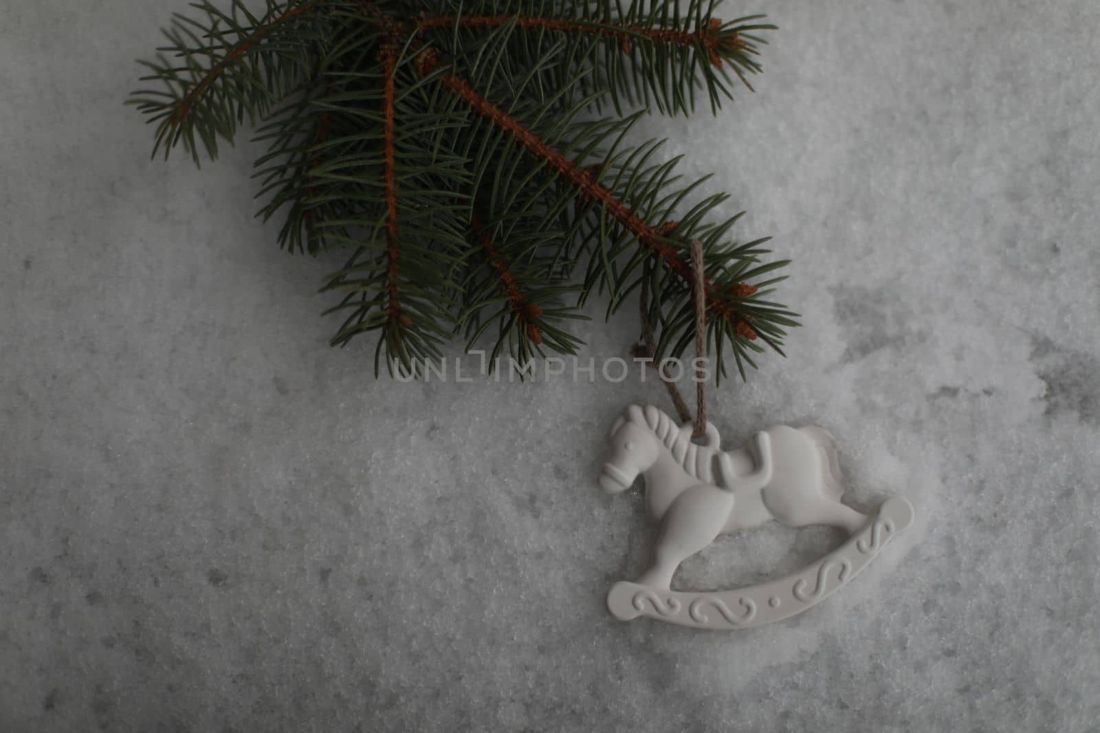 Christmas toy horse hanging on a green branches in the snow in winter. Christmas tree, toy horse, gift. New Year decor.