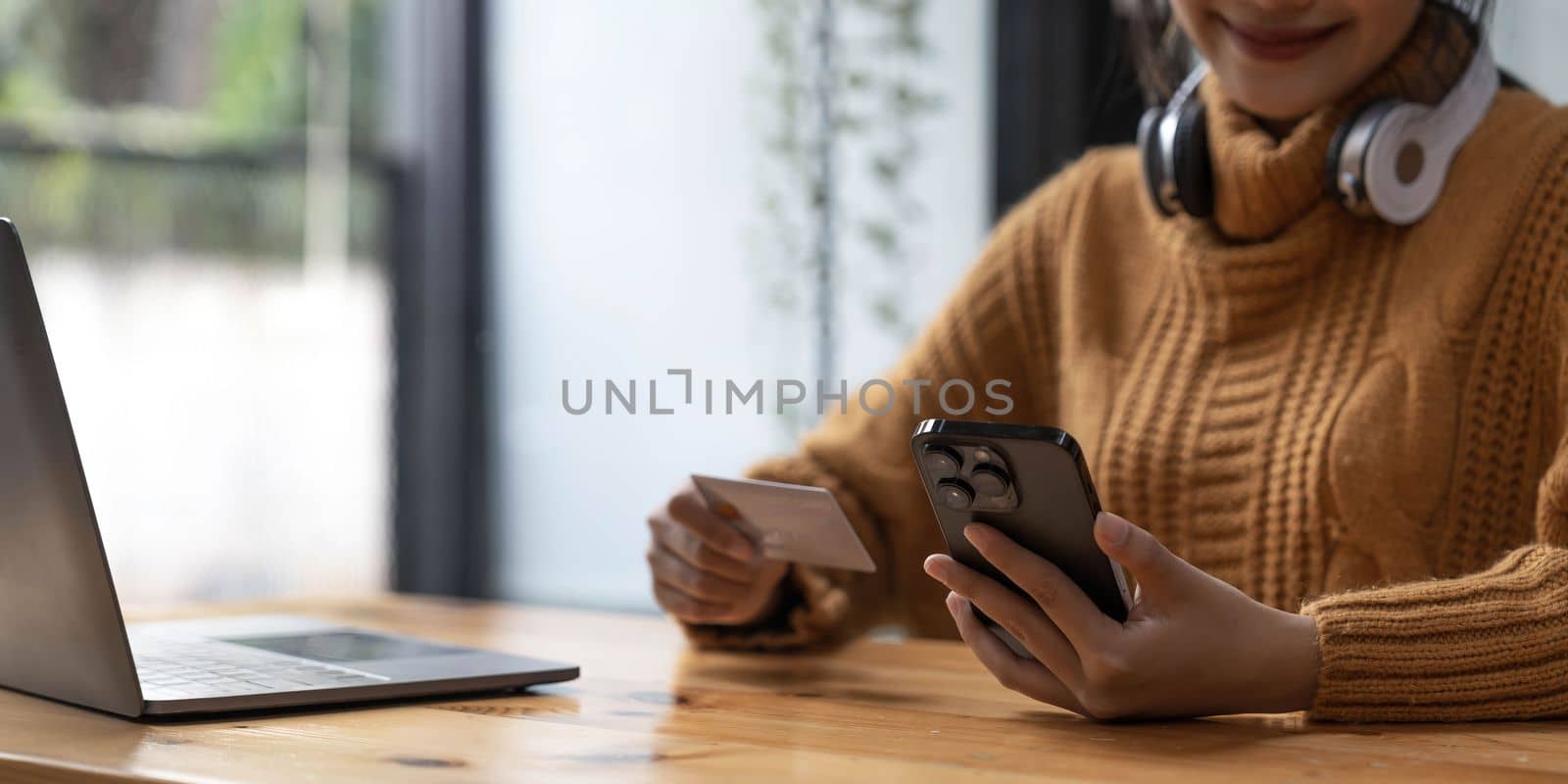 Attractive Asian female sits at her desk, holding a smartphone and a credit card. close-up image. Online payment, credit card payment, mobile banking, online shopping, cashless society...