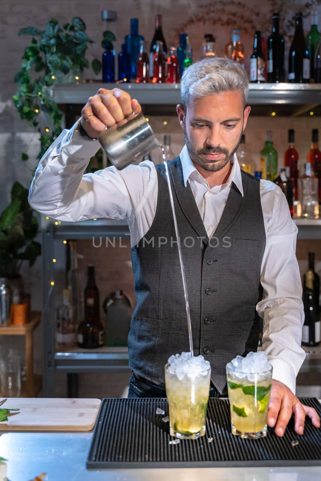Barman making cocktail Mojito in night club adding ingredients and creating expert drinks on bar counter. High quality photo