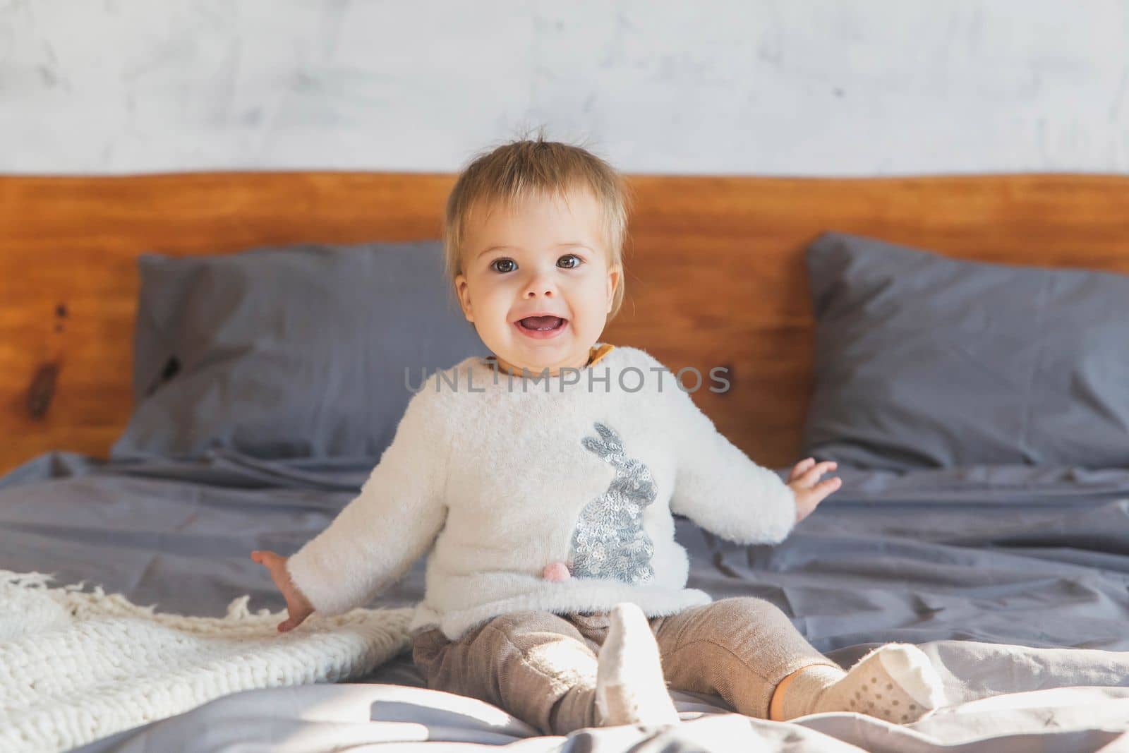 Cute baby lies on the bed and laughs so that two teeth are visible.