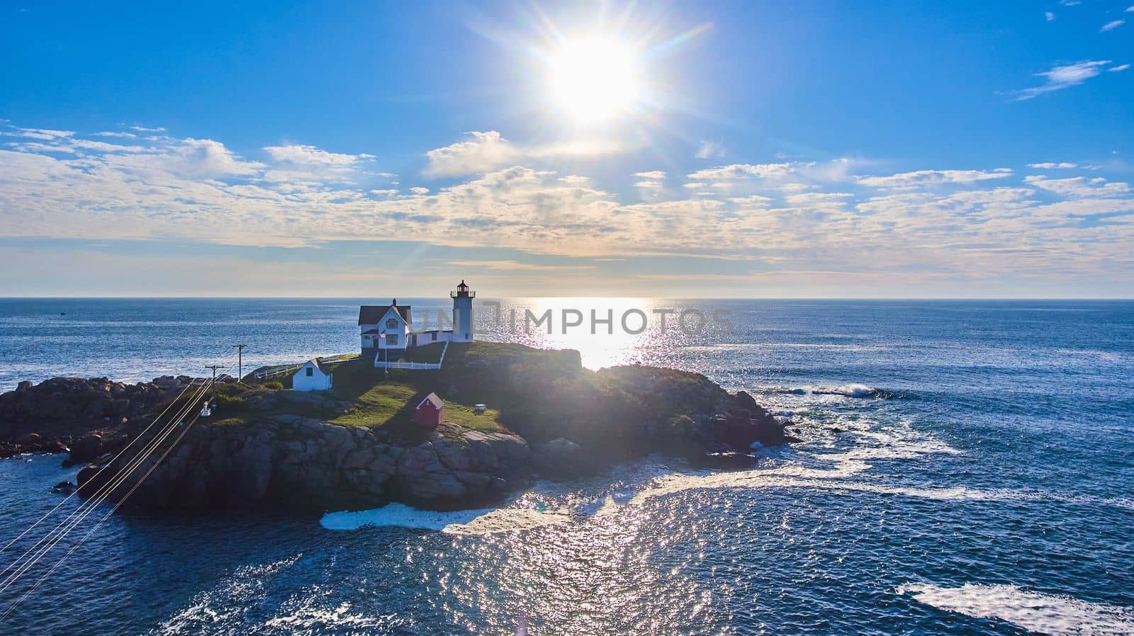 Small Maine island with lighthouse from above with sun shining over ocean by njproductions