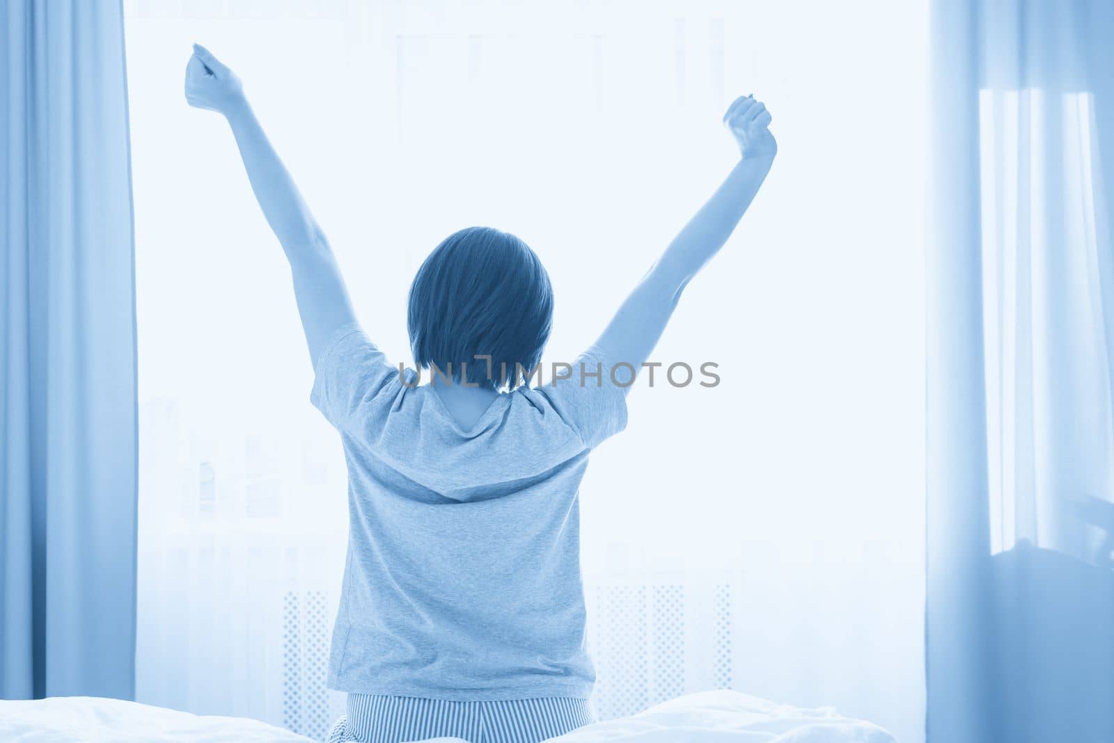 Girl stretching in bed after wake up, back view by Mariakray