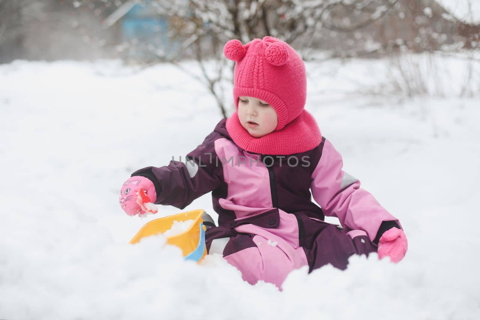 Adorable girl dig snow with shovel and pail on playground covered with snow. little girl playing in the snow.