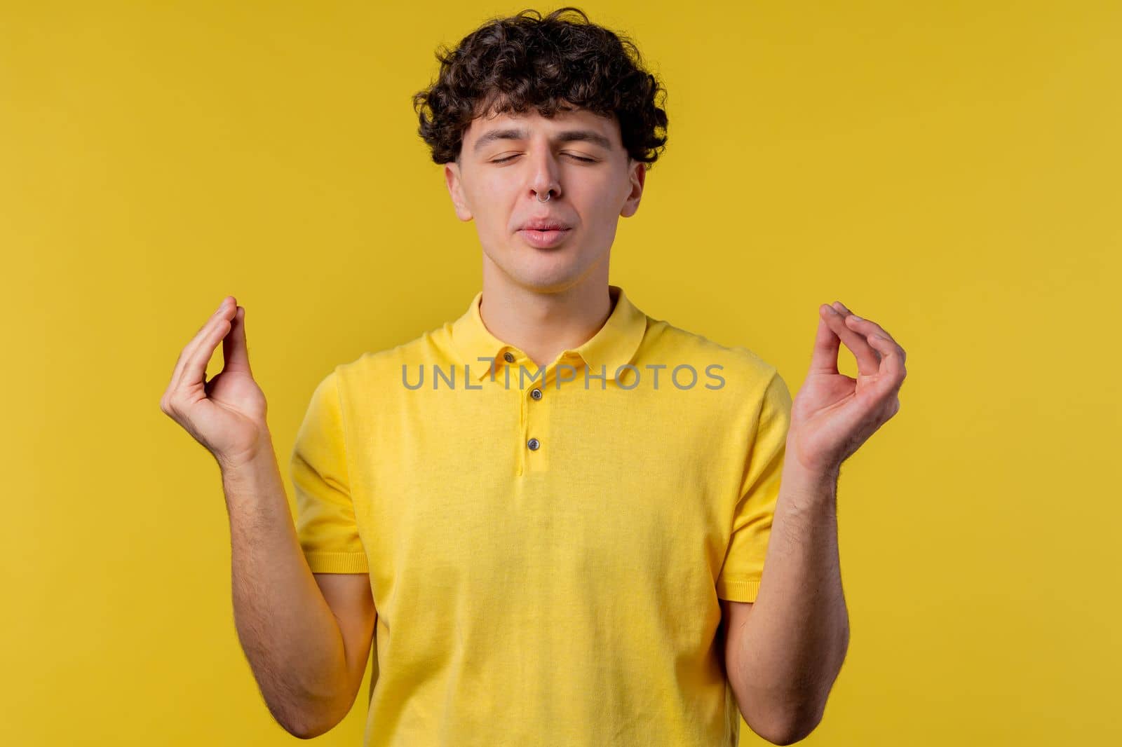 Calm man relaxing, meditating, refuses stress. Curly haired guy breathes deeply, calms down yellow studio background. Yoga, moral balance, zen concept. by kristina_kokhanova