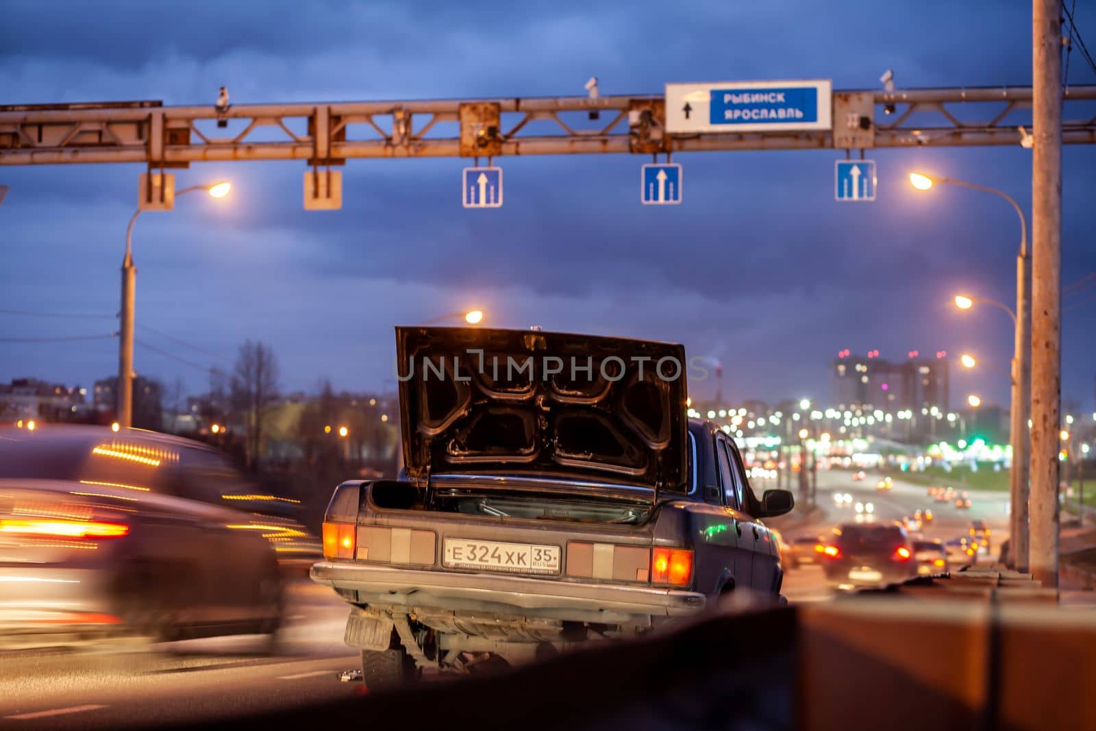 29.11.2022, Cherepovets, Russia.A large automobile bridge on which cars drive at night. There is a broken car and an emergency sign on the bridge. A bridge with large columns and lighting. 