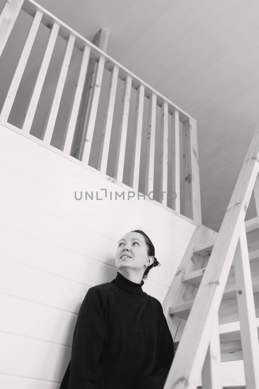 Young woman sitting on wooden stairs in modern house. Attractive brunette at home. Black and white
