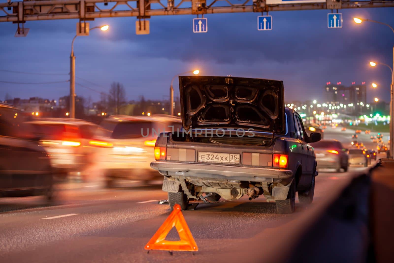 29.11.2022, Cherepovets, Russia. A large automobile bridge on which cars drive at night. There is a broken car and an emergency sign on the bridge. A bridge with large columns and lighting. 