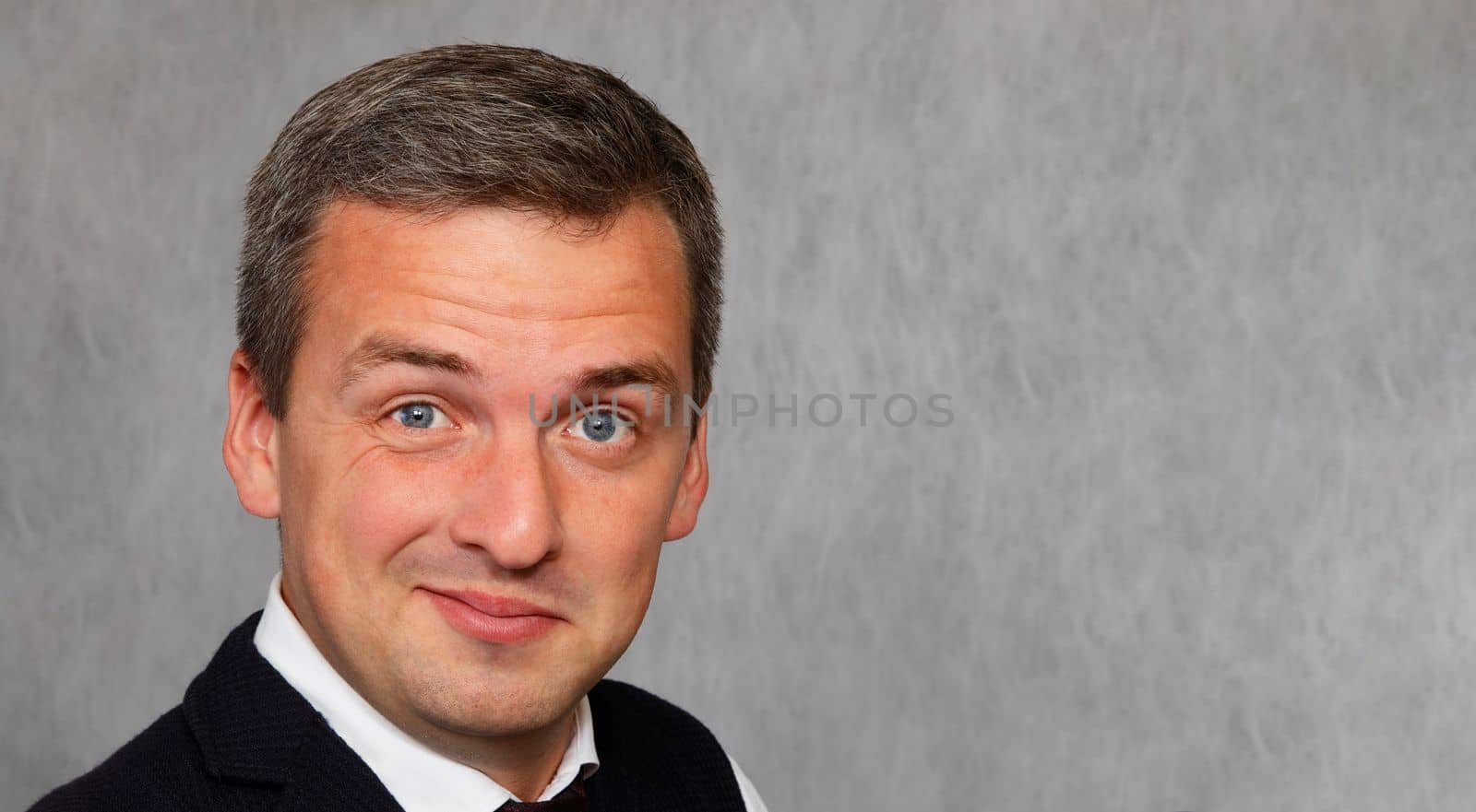 Smiling face of a businessman 30-35 years old close-up on a gray background. The handsome man smiles sarcastically.