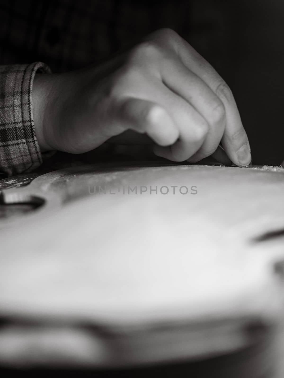 artisan working on raw wood violin plate with finger plane on the bench