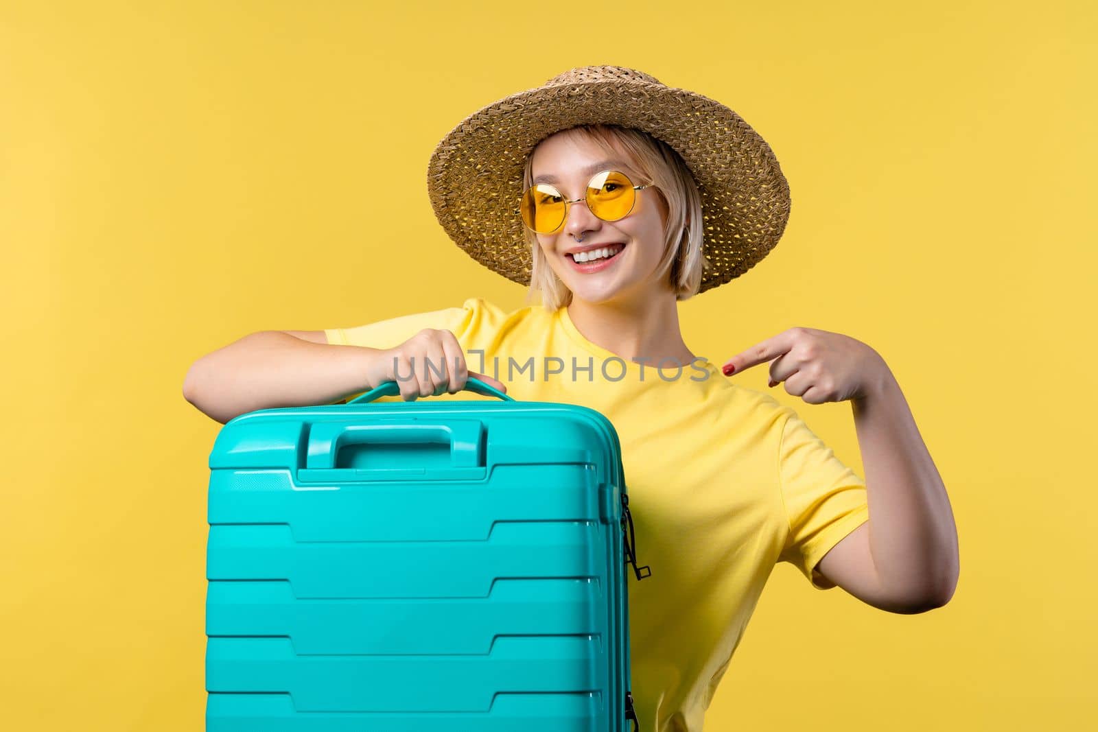 Young pretty woman with carry-on suitcase on yellow background. Teenager traveling with blue luggage bag for airplane hand baggage. Summer travel, vacation concept. High quality photo