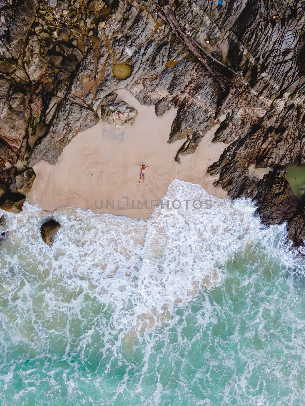 Drone aerial view at Freedom beach in Phuket Thailand, men laying down on beach in bay by fokkebok