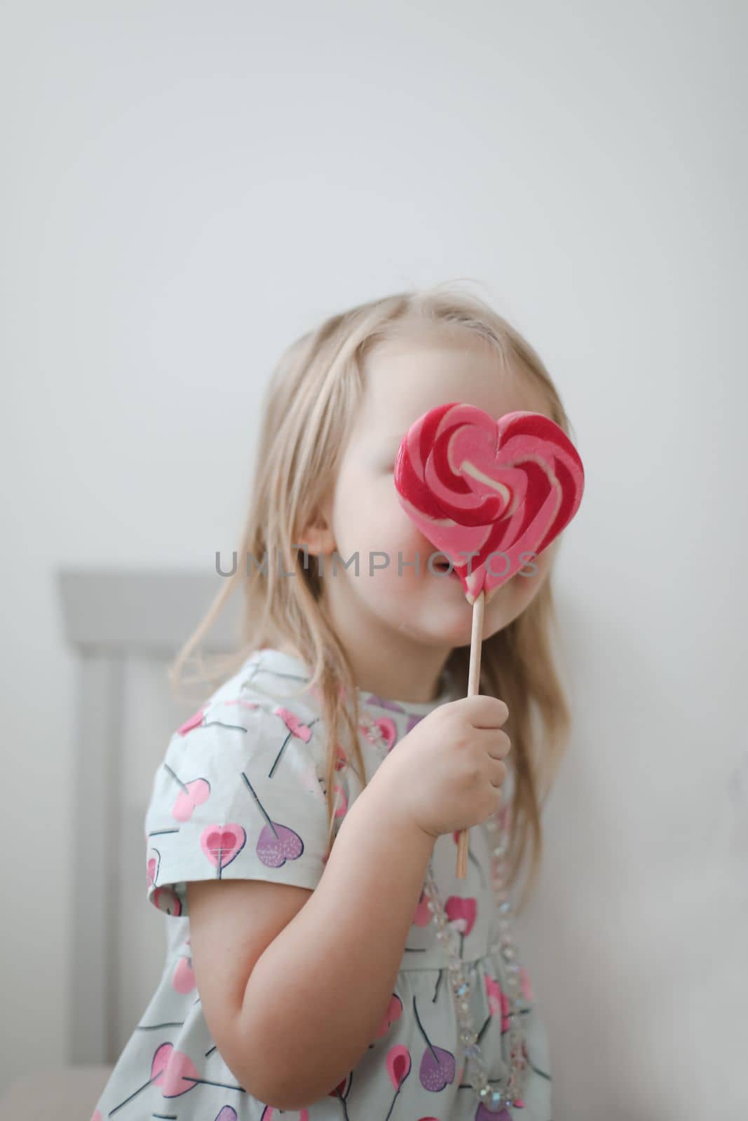 Beautiful little girl holding a big heart shaped lollipop.