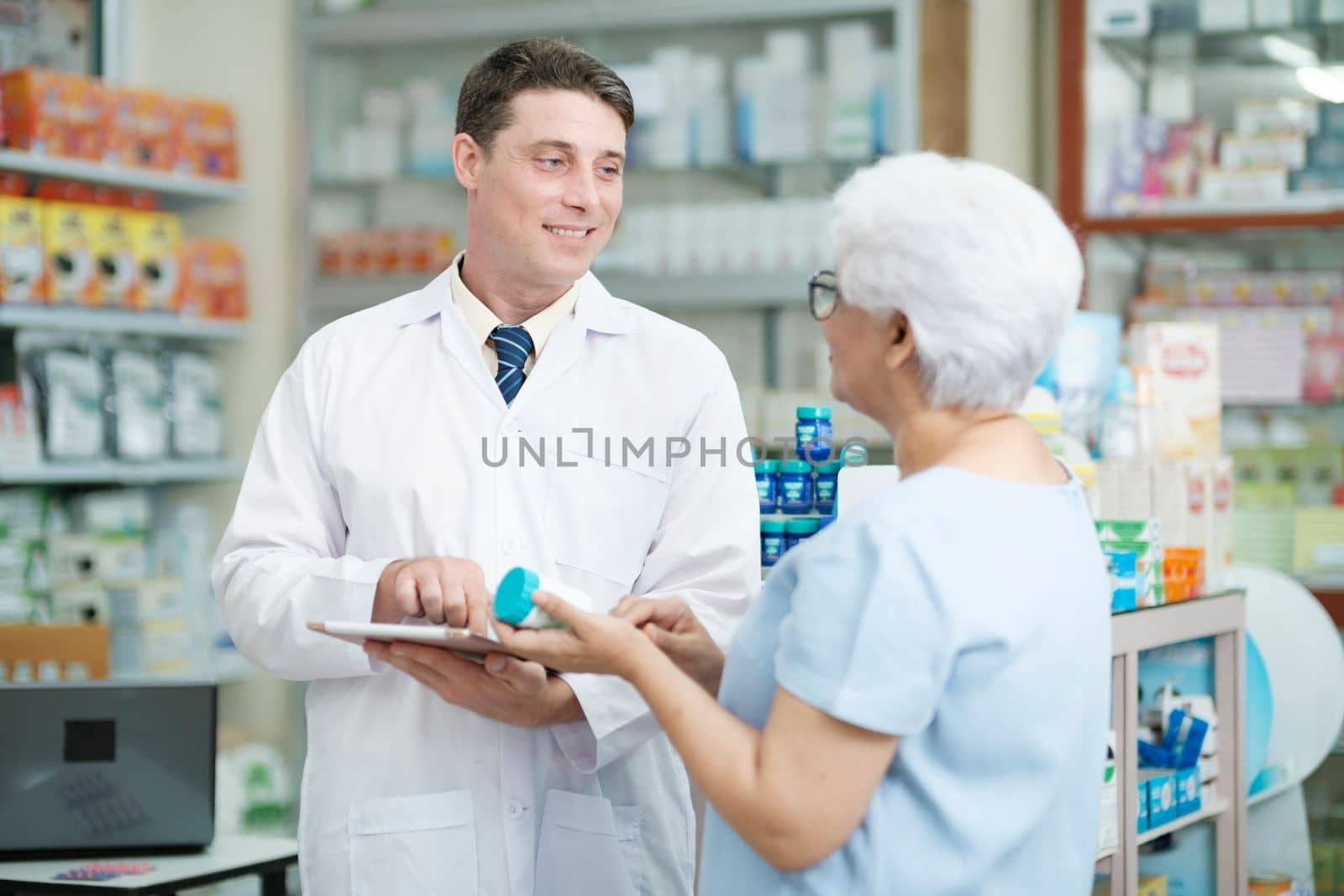 Smart male pharmacist at the drugstore wearing white gown talking, giving advice, explaining, suggesting, and recommending to client or patient about the prescription and medications. Medicine and healthcare concept.