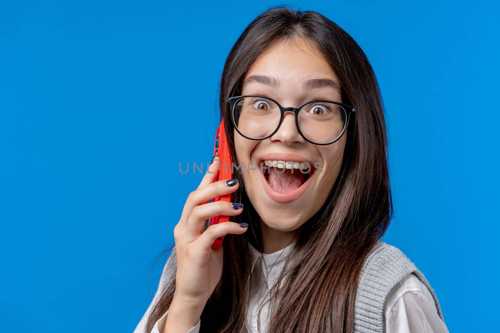 Surprised schoolgirl have surprise talk with friend by phone, nice joke. Young woman with open mouth on blue background. Having phone call. . High quality photo