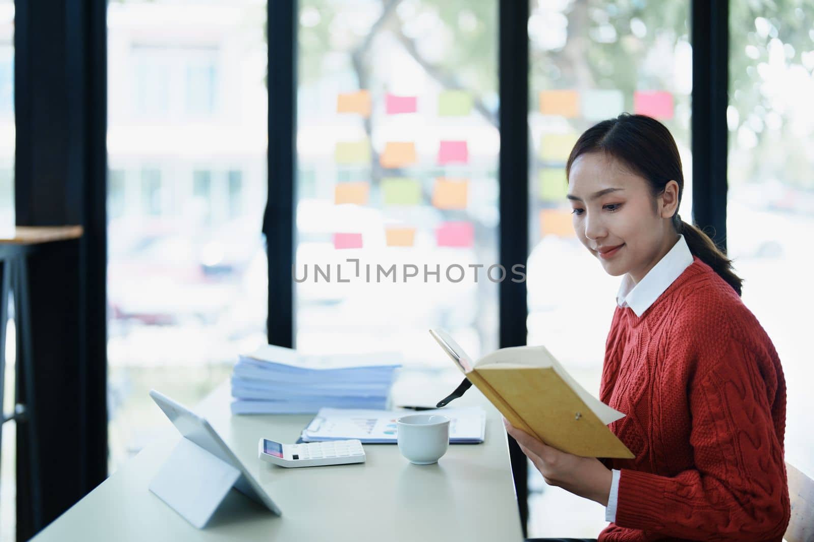 Portrait of a thoughtful Asian businesswoman looking at financial statements and making marketing plans using a computer with notebook on her desk.