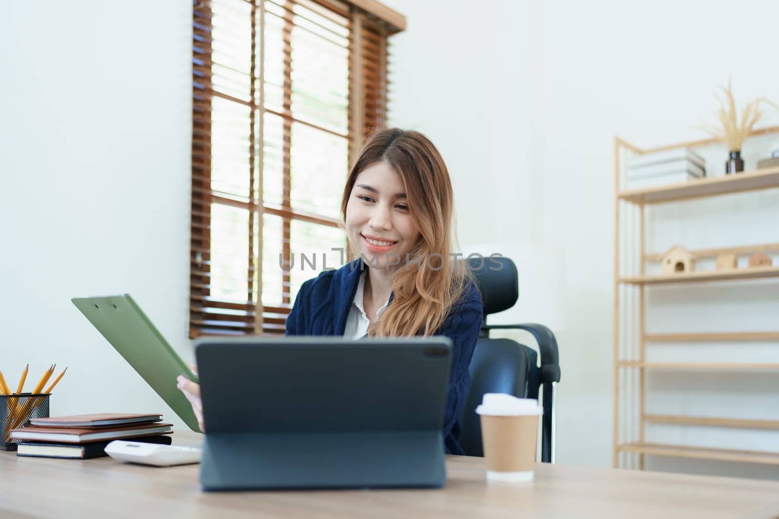 Portrait of a thoughtful Asian businesswoman looking at financial statements and making marketing plans using a computer on her desk.