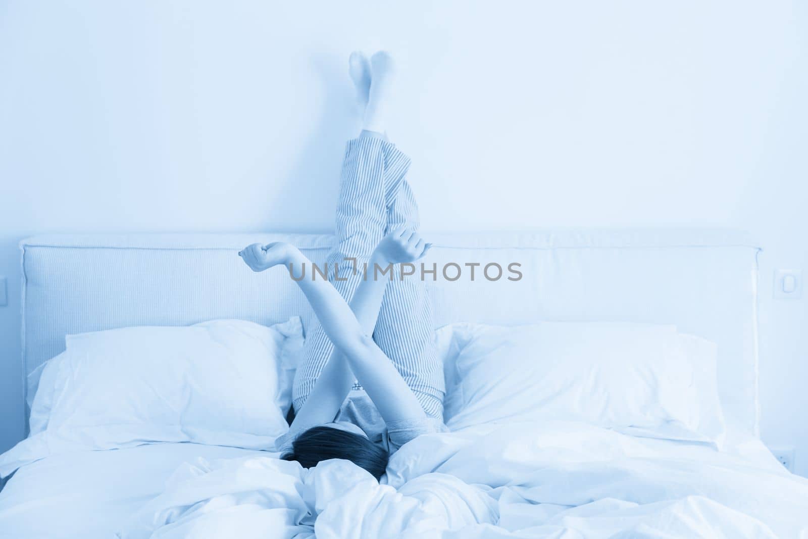 Woman stretching in bed with legs raised up high in bedroom by Mariakray