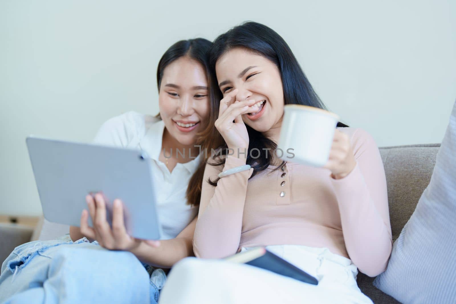 lgbtq, lgbt concept, homosexuality, portrait of two asian women posing happy together and loving each other while playing tablet at sofa by Manastrong