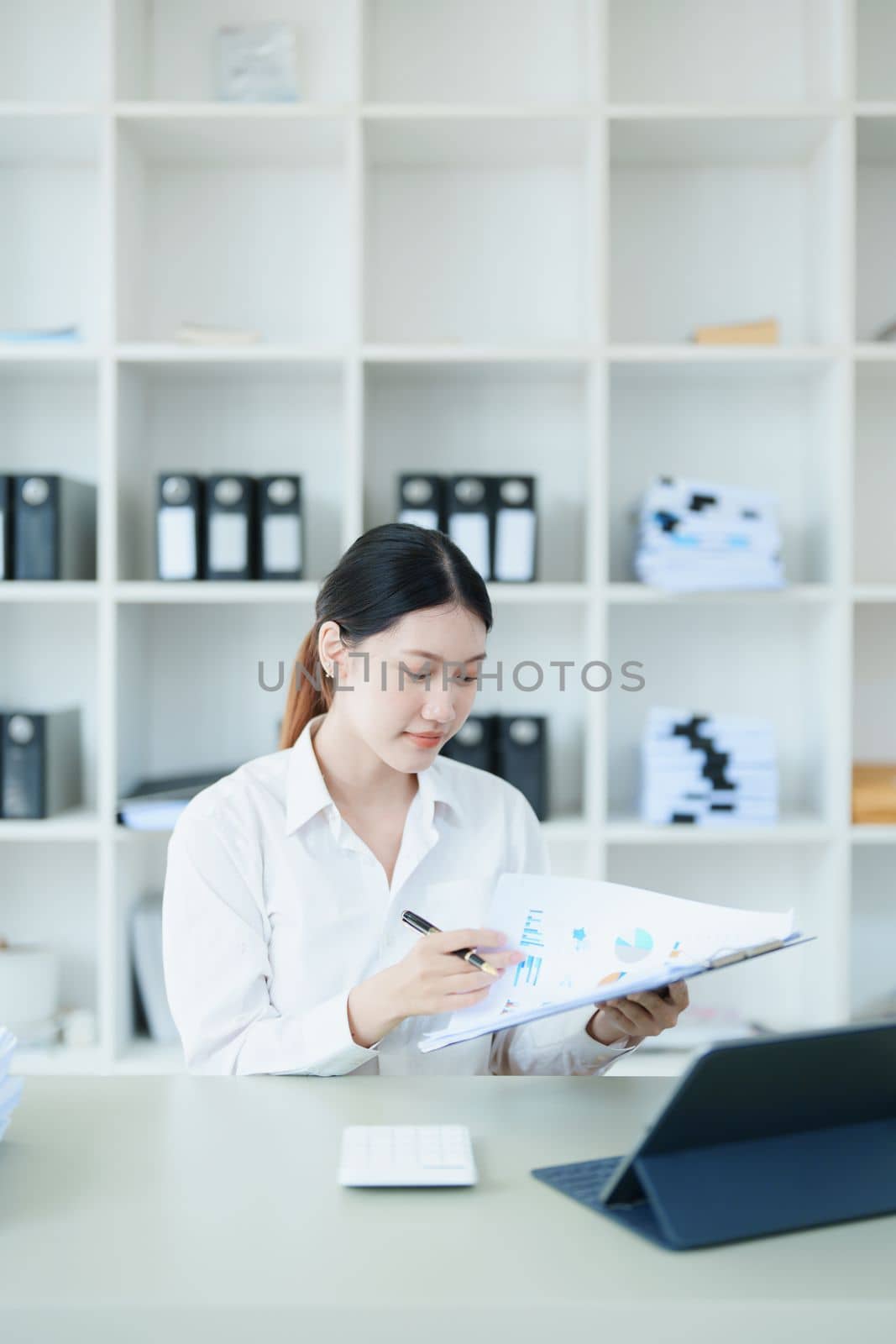 Portrait of a thoughtful Asian businesswoman looking at financial statements and making marketing plans using a computer on her desk.