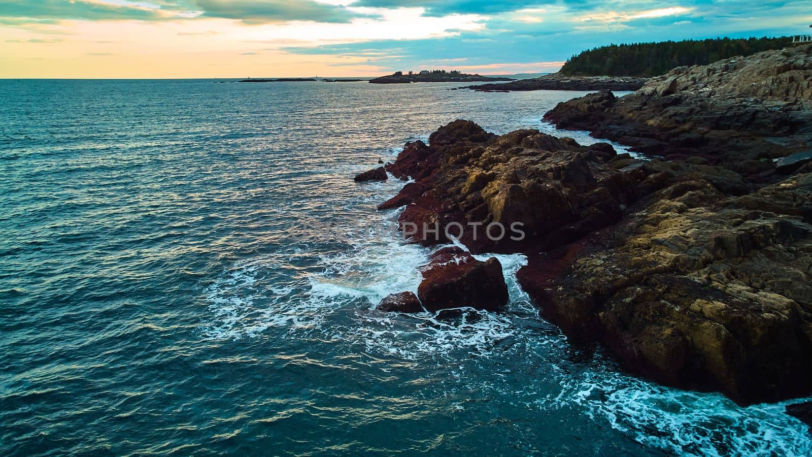 Serene ocean view over coasts of Maine with rocky coasts, waves crashing, and sunset light by njproductions