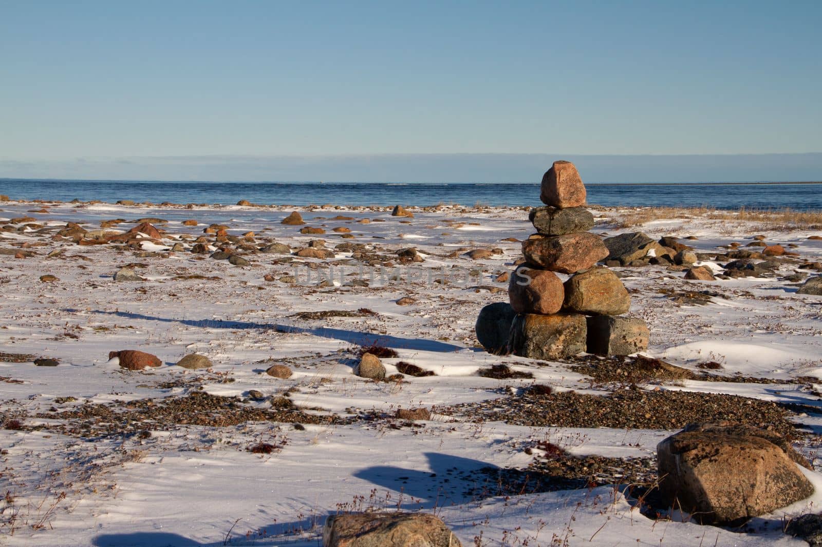 Arctic landscape - an Inuksuk or Inukshuk landmark on a snow covered arctic tundra in Nunavut on a clear sunny day, near Arviat, Nunavut, Canada