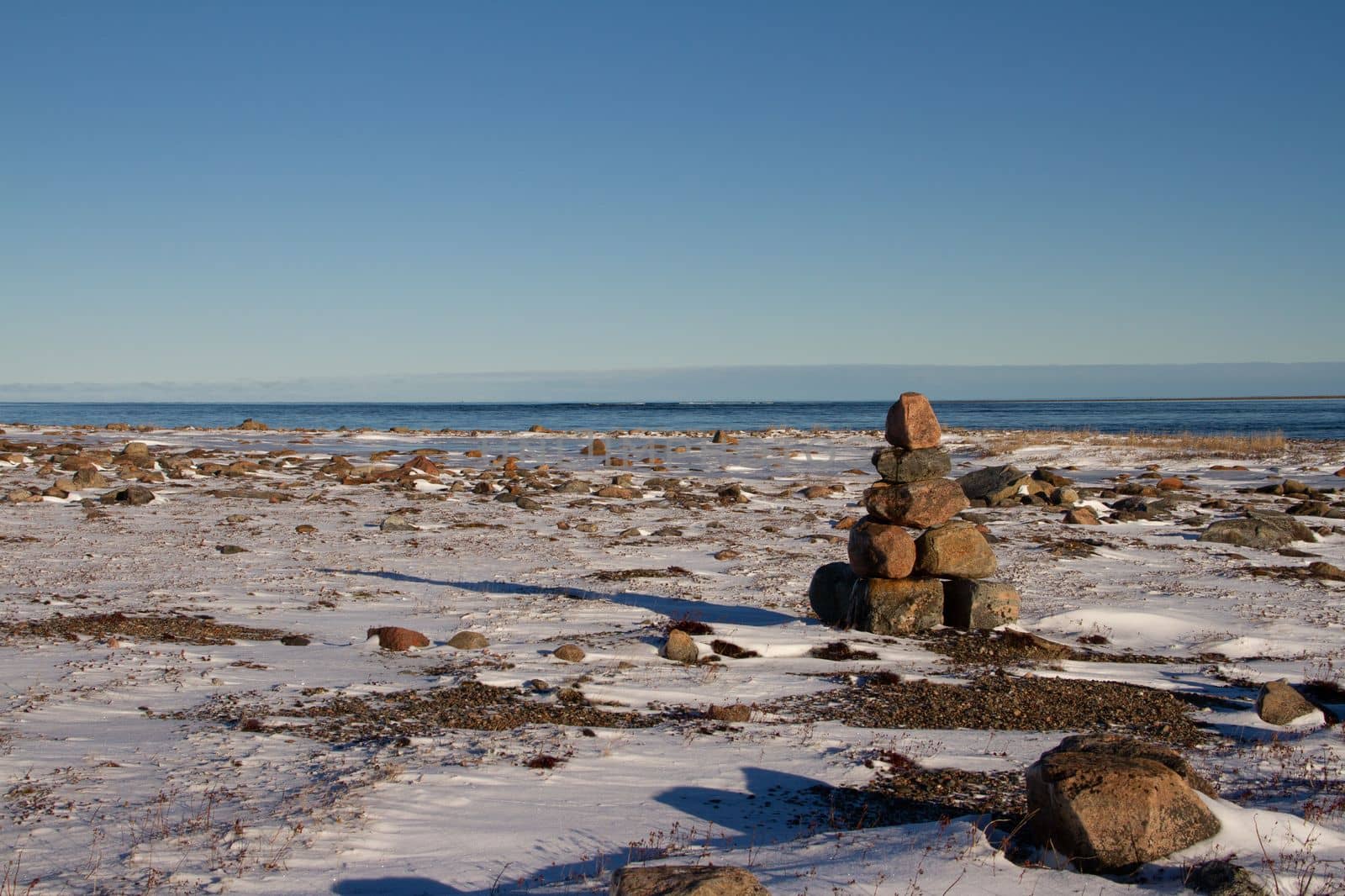 Arctic landscape - an Inuksuk or Inukshuk landmark on a snow covered arctic tundra in Nunavut on a clear sunny day by Granchinho