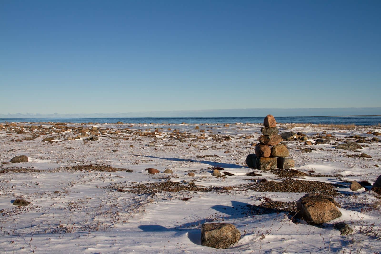 Arctic landscape - an Inuksuk or Inukshuk landmark on a snow covered arctic tundra in Nunavut on a clear sunny day by Granchinho