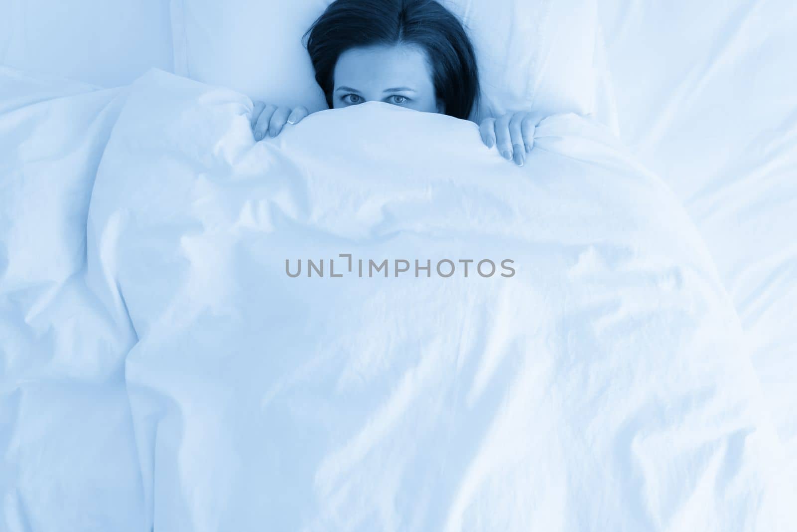 young beautiful woman in bed hiding under duvet by Mariakray