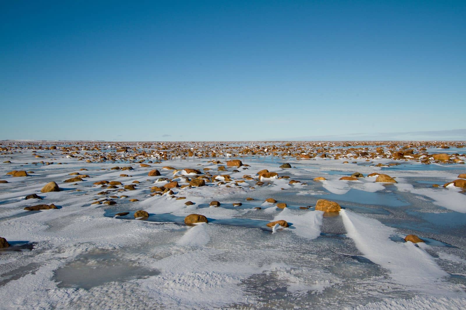 Arctic landscape - frozen arctic tundra in Nunavut over a rocky snow covered waterbody on a clear cold day, near Arviat, Nunavut