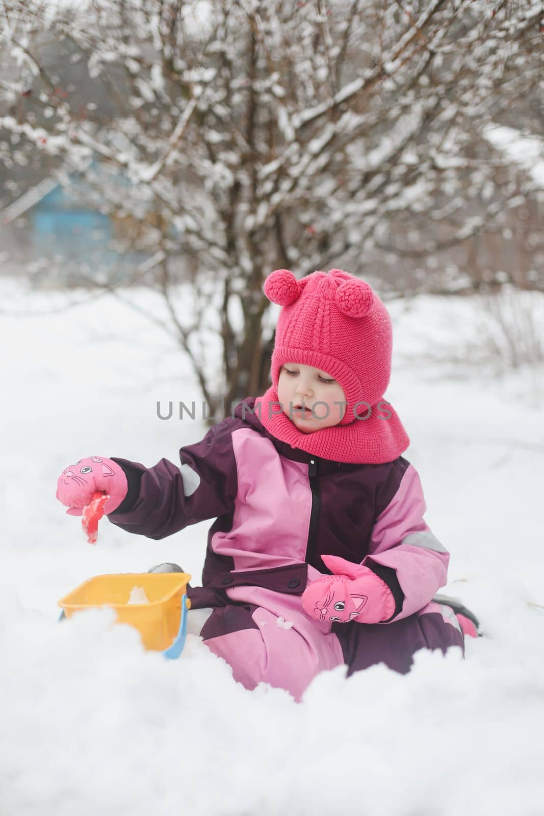 Adorable girl dig snow with shovel and pail on playground covered with snow. little girl playing in the snow.