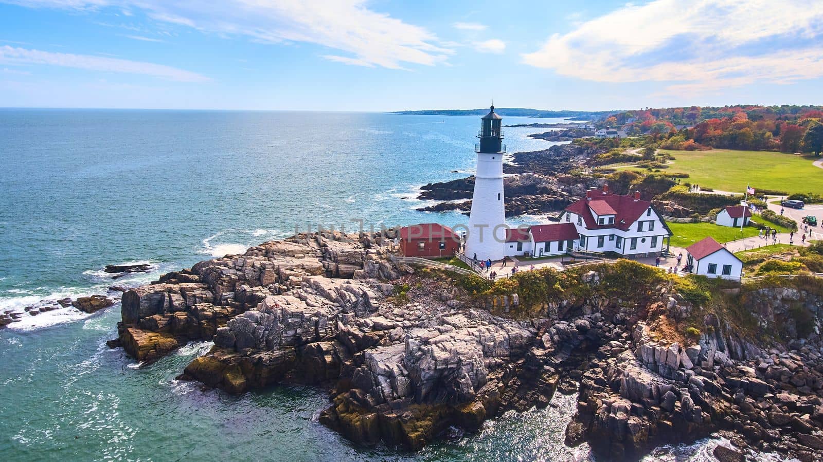 Aerial view of Maine coastline with rocky cliffs and iconic white lighthouse by njproductions