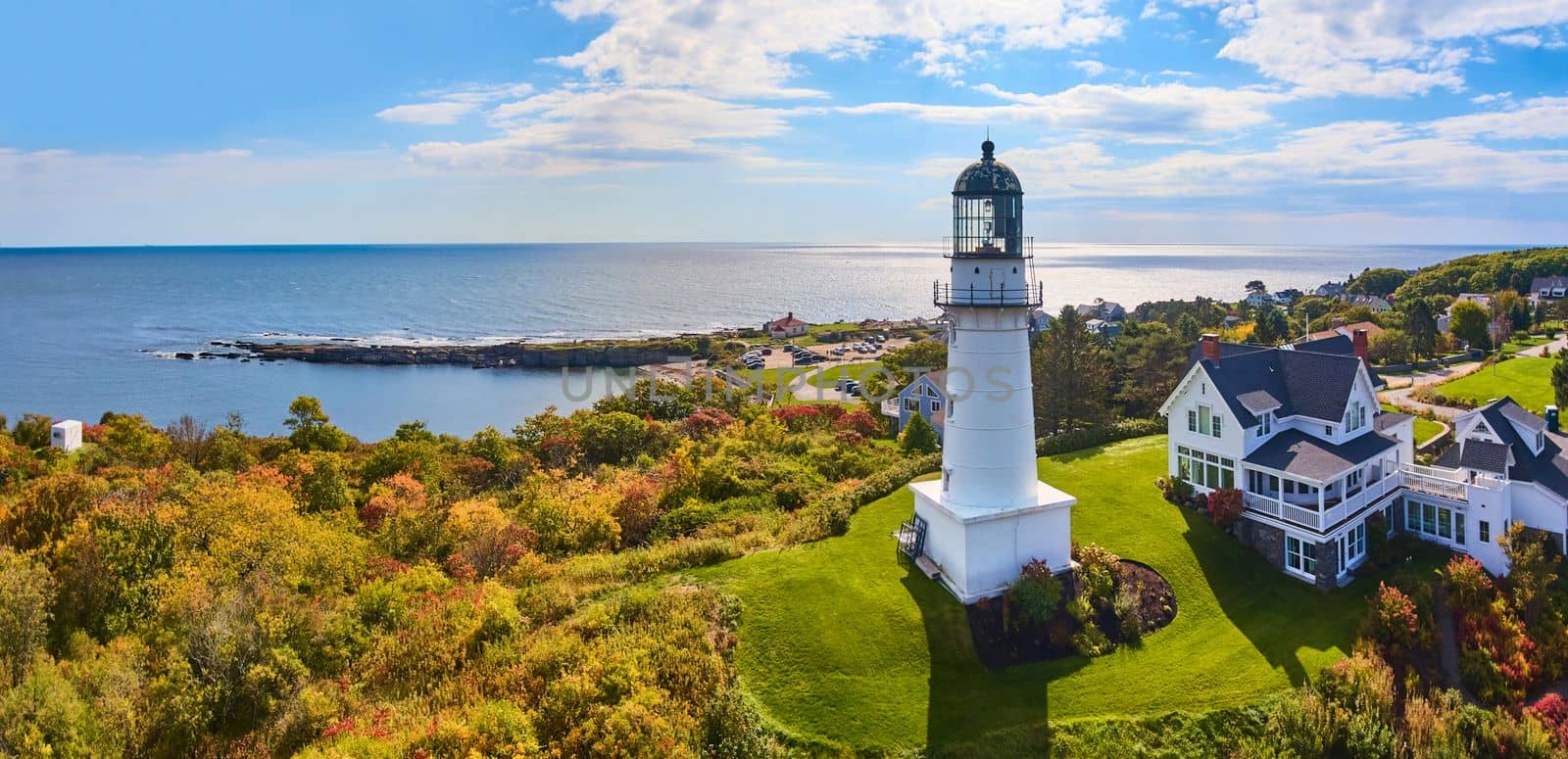 Image of Lighthouse on hill with house overlooking stunning Maine coastline in fall